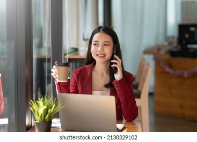 Confident beautiful Asian woman talking on the phone while holding a coffee at café.