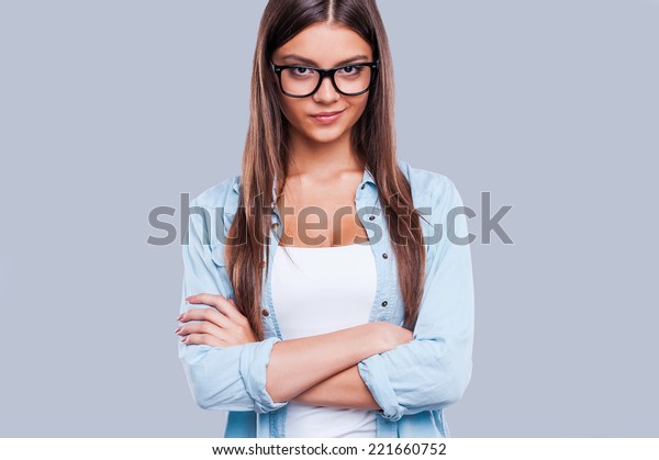 Confident beauty.\
Confident young women keeping arms crossed and smirking while\
standing against grey\
background