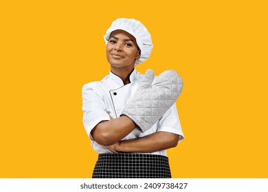 Confident black female chef with crossed arms wearing an oven mitt, african american cook woman embodying professional readiness, standing against yellow background, signaling kitchen competence - Powered by Shutterstock