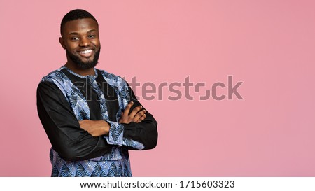 Confident black man in traditional african clothes with arms crossed posing over pink, panorama with copy space