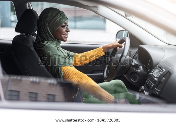 Confident Black Muslim Female In Hijab Driving Car\
In City, Smiling African Islamic Female Driver In Headscarf\
Enjoying Road Drive In Her New Modern Automobile, Side View Shot\
Through Window