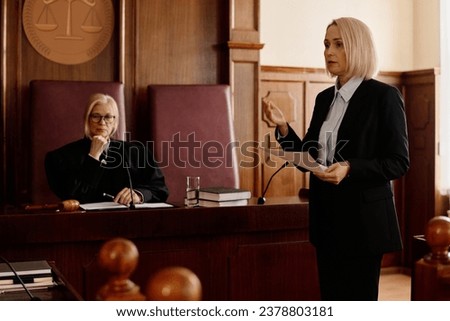 Confident blond female prosecutor looking at suspect and his attorney
