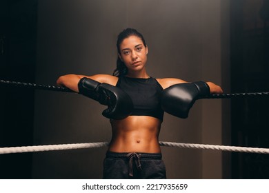 Confident boxer looking at the camera while leaning against the ropes of a boxing ring in a gym. Female boxer getting ready for a boxing match. - Powered by Shutterstock