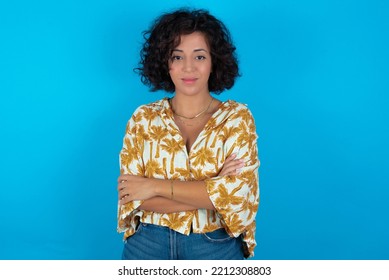 Confident Brunette Arab Woman Wearing Hawaiian Shirt Over Blue Background With Arms Crossed Looking To The Camera