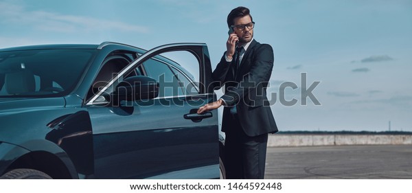 Confident\
business expert. Full length of handsome young businessman talking\
on the phone while entering his car\
outdoors