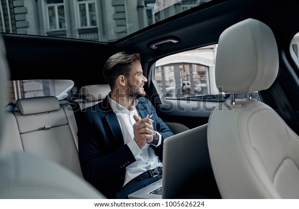 Confident business\
expert. Handsome young man in full suit looking through the window\
while sitting in the\
car