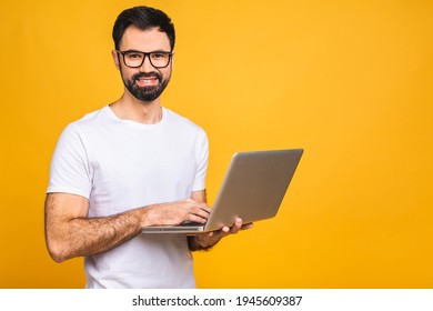 Confident business expert. Confident young handsome bearded man in casual holding laptop and smiling while standing over isolated yellow background. 