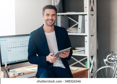 Confident Business Expert. Confident Young Man Holding Digital Tablet And Smiling While Leaning At The Deck In Office