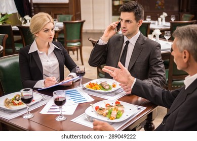 Confident business partners in suits discussing contract during business lunch.