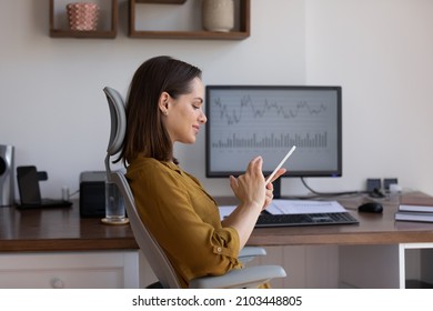 Confident business professional finance trader woman using app on smartphone, sitting at desktop monitor with trading infographics, charts, rates, chatting online, getting income, profit, smiling - Powered by Shutterstock