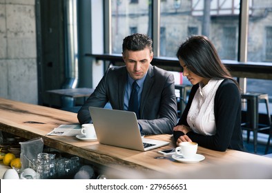 Confident Businessman And Attractive Businesswoman Working On Laptop Together In Cafe