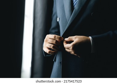 Confident businessman buttoning or adjust classic blue suit near window in hotel room at the morning. Handsome man wearing a nice suit on wedding day. - Powered by Shutterstock