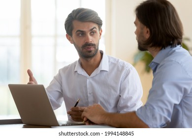 Confident businessman discussing project strategy with business partner, mentor coach training trainee, using laptop, pointing at screen, helping with software, coworkers working together