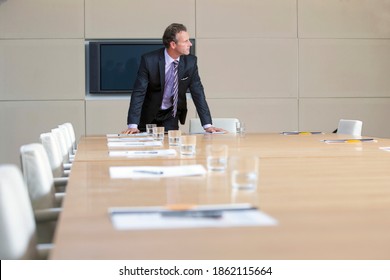 A confident Businessman in a formal suit leaning on the table in an empty conference room - Powered by Shutterstock