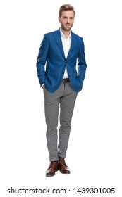 Confident businessman holding both hands in his pockets while wearing a suit and standing on white studio background