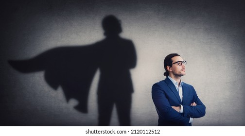 Confident Businessman Looking Determined As Casting A Powerful Superhero Shadow On The Wall. Motivated And Ambitious Business Person Shows Inner Strength. Hero Leadership And Power Concept