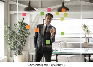 Confident businessman looking at glass wall with colorful sticky papers in office, executive manager team leader working on corporate project plan or strategy, reading notes on tasks on stickers - Powered by Shutterstock