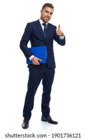 Confident Businessman In Navy Blue Suit Making Thumbs Up Gesture And Holding Clipboard, Smiling And Standing Isolated On White Background In Studio, Full Body