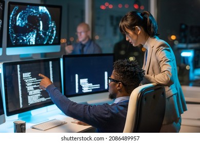 Confident businessman pointing at coded data on computer screen while explaining it to female colleague at meeting