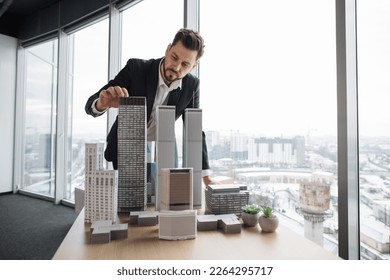 Confident businessman real estate agents in black stylish formal suit standing while touching 3d model skyscraper of city architecture design at office with panoramic city view. - Powered by Shutterstock