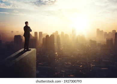Confident businessman standing on the building rooftop while looking at the silhouette of cityscape at dusk time - Shutterstock ID 1927300793