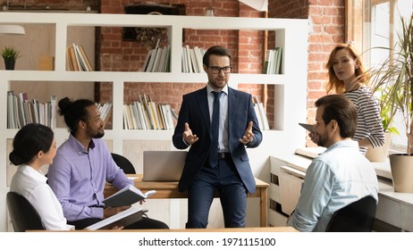 Confident Businessman In Suit And Glasses Leading Briefing, Business Coach Mentor Training Diverse Employees, Team Sharing Ideas, Negotiating Project Strategy At Corporate Meeting In Office