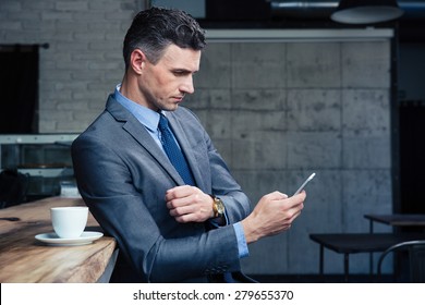 Confident businessman in suit using smartphone in cafe