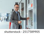 Confident businessman using an ATM outside, smiling at the camera. The setting features modern office buildings with people walking in the background, emphasizing convenience and technology.