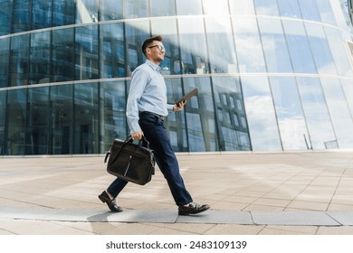 Confident businessman walking with a briefcase and tablet, near modern glass office buildings. - Powered by Shutterstock