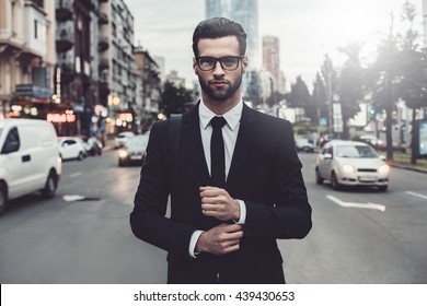 Confident businessman. Confident young man in full suit adjusting his sleeve and looking away while standing outdoors with cityscape in the background - Shutterstock ID 439430653