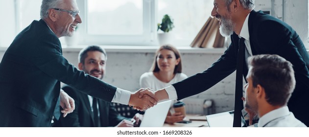 Confident businessmen shaking hands and smiling while working together with colleagues in the board room - Shutterstock ID 1669208326