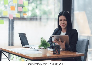 Confident Businesswoman Analyzing Data:  A focused and confident businesswoman works on her laptop and tablet at a modern office desk, surrounded by graphs and charts. - Powered by Shutterstock