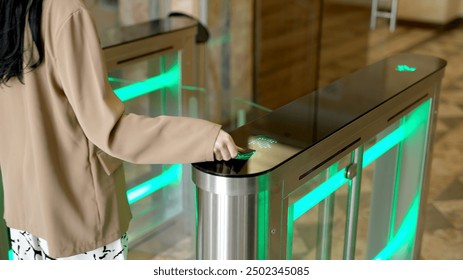 A confident businesswoman effortlessly passes through a modern turnstile using her personal access card in a sleek office lobby. Ideal for concepts of advanced security, workplace technology.