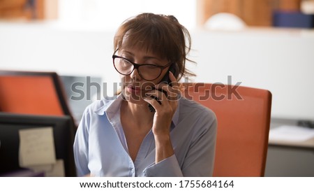 Confident businesswoman in glasses consulting client on cellphone in office, busy employee solving business problem online, having serious conversation, phone negotiations, horizontal photo