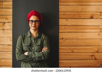 Confident Businesswoman Looking At The Camera While Standing Against A Wall With Her Arms Crossed. Muslim Businesswoman Wearing A Headscarf In A Modern Workplace.