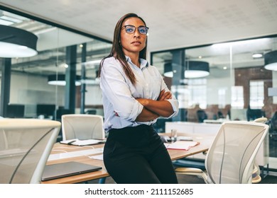 Confident businesswoman looking thoughtful in a modern office. Mid-adult businesswoman leaning on a table with her arms crossed. Female entrepreneur wearing business casual in a boardroom. - Powered by Shutterstock