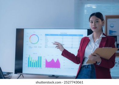 Confident businesswoman in modern office presenting charts on screen, explaining data analysis. Focus on growth and planning using technology for communication and decision-making - Powered by Shutterstock