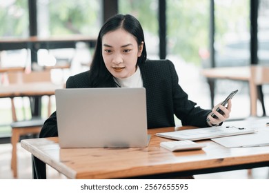 Confident businesswoman multitasking with a laptop and phone in a stylish cafe setting, showcasing remote work and modern technology. - Powered by Shutterstock