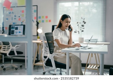 Confident businesswoman multitasks in a modern office, answering calls and taking notes with a smile, showcasing her tech-savvy approach to work - Powered by Shutterstock