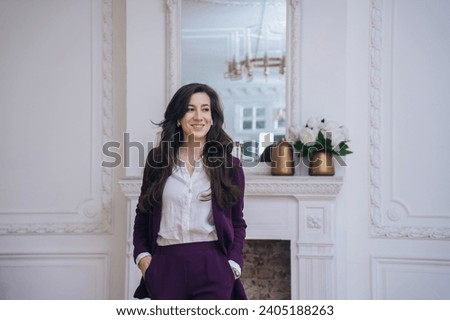 Confident businesswoman in a purple suit with a pleasant smile, standing in a room with classic white decor and a fireplace