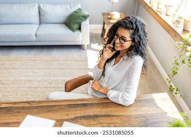 Confident businesswoman sitting at a desk, smiling and engaged in a phone call. Bright, modern office setting with natural light and stylish decor, creating a professional and pleasant atmosphere. - Powered by Shutterstock