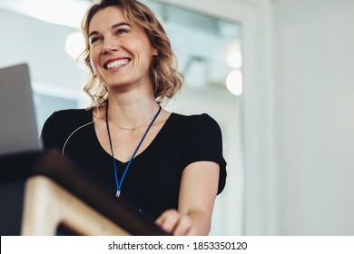 Confident businesswoman standing at podium. Smiling female business professional addressing a conference. - Powered by Shutterstock