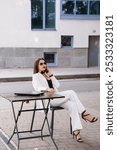 A Confident Businesswoman in Striped Suit Relaxing at a Streetside Table.