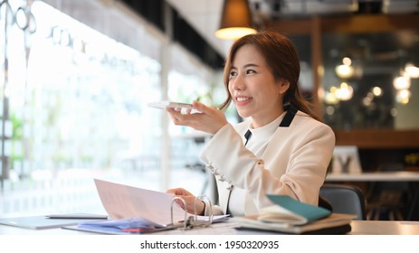 Confident Businesswoman Talking By Speakerphone While Sitting In Modern Office.