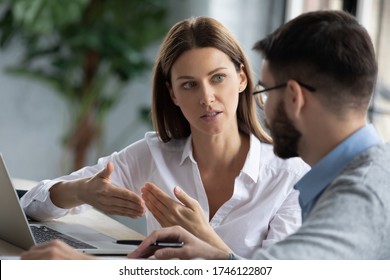 Confident businesswoman training intern, helping with corporate software to new employee, using laptop, sitting at office desk together, colleagues working on online project together close up
