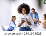 Confident businesswoman using a tablet in a modern office environment. Colleagues engage in a discussion in the background, highlighting teamwork and technology in a professional setting.