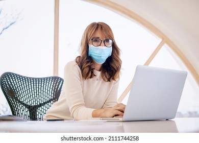 Confident businesswoman wearing face mask while working on laptop at the office.  - Powered by Shutterstock