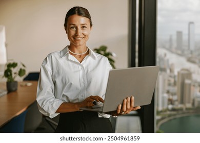 A confident businesswoman is working in a modern office with a stunning city view - Powered by Shutterstock