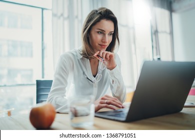 Zuversichtliche Geschäftsfrau, die an ihrem Arbeitsplatz in einem modernen Büro mit Laptop arbeitet.Unscharfer Hintergrund