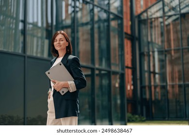 A confident businesswoman is working on a laptop outside a contemporary office building - Powered by Shutterstock